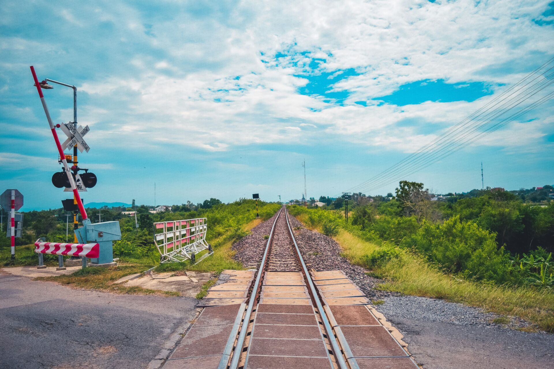 Railway crossing with green surrounds and partly cloudy sky
